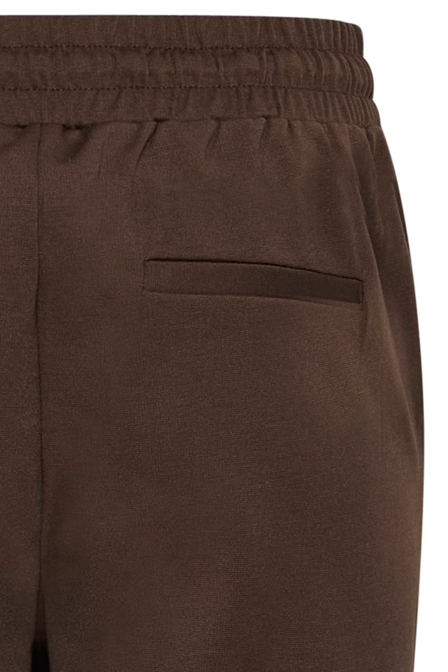 Close-up of dark brown trousers showing the elastic waistband and a side welt pocket.