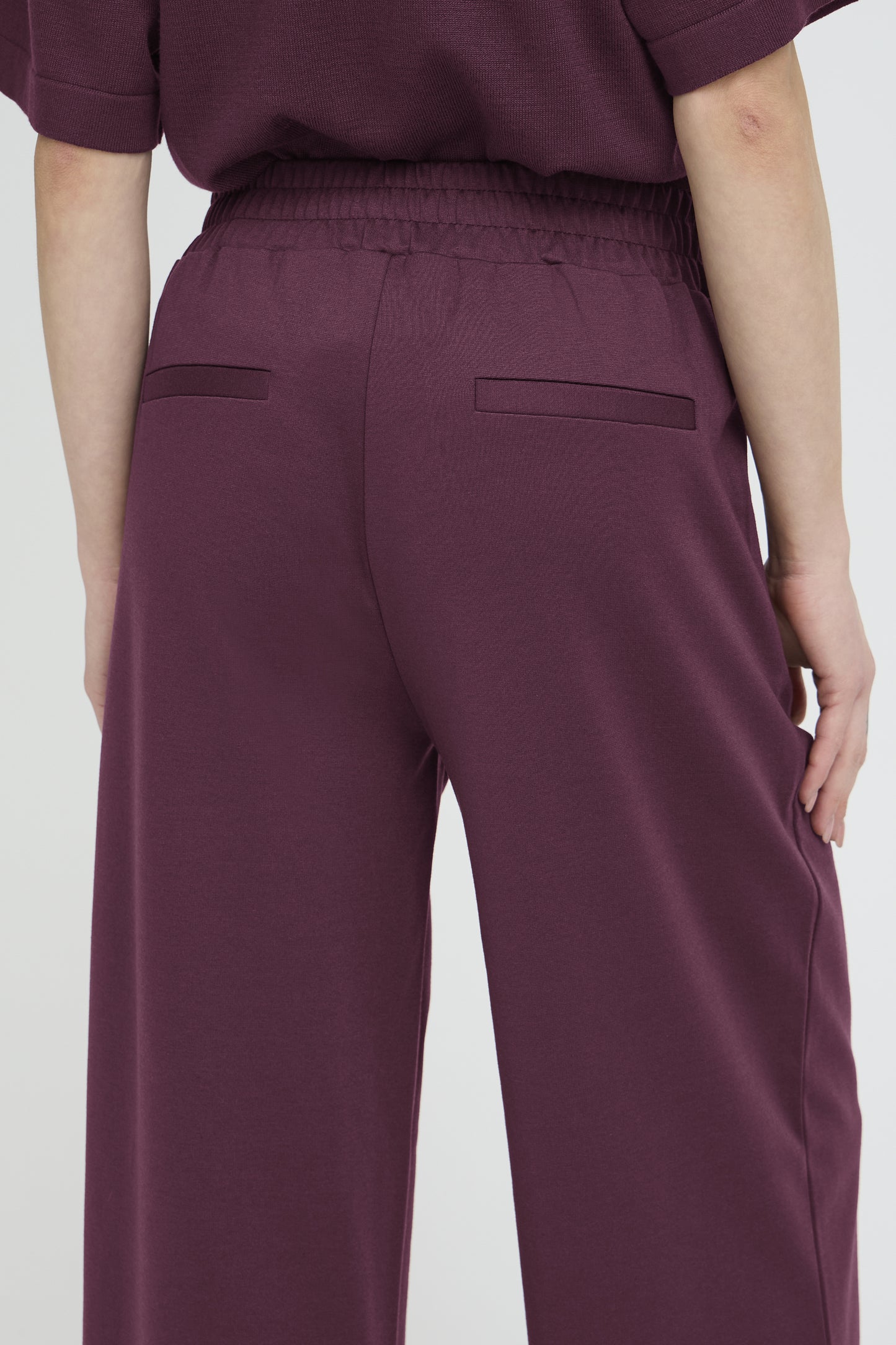 Close-up back view of a person wearing wide-leg trousers in a deep plum purple color, paired with a matching top.