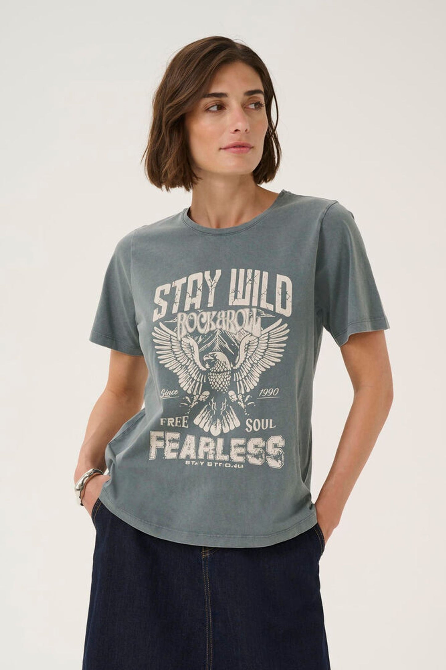 Woman wearing a gray t-shirt with an eagle graphic and text on a plain background