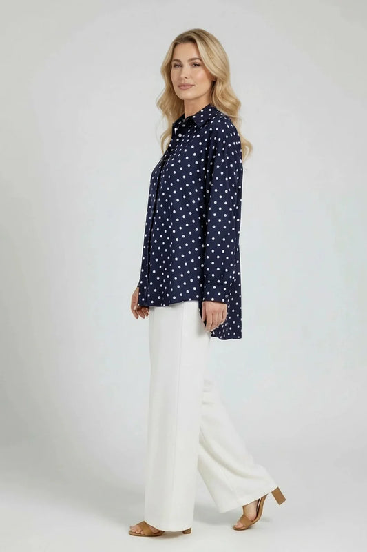 Woman wearing a navy polka dot blouse and white pants on a white background