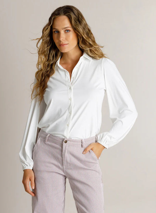 A woman modeling a white long-sleeve button-up shirt tucked into light pink and white vertically striped trousers, set against a plain light beige studio background.