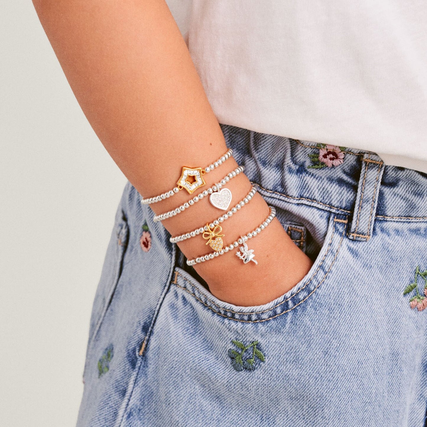 Person wearing multiple bracelets on a wrist with a denim jacket