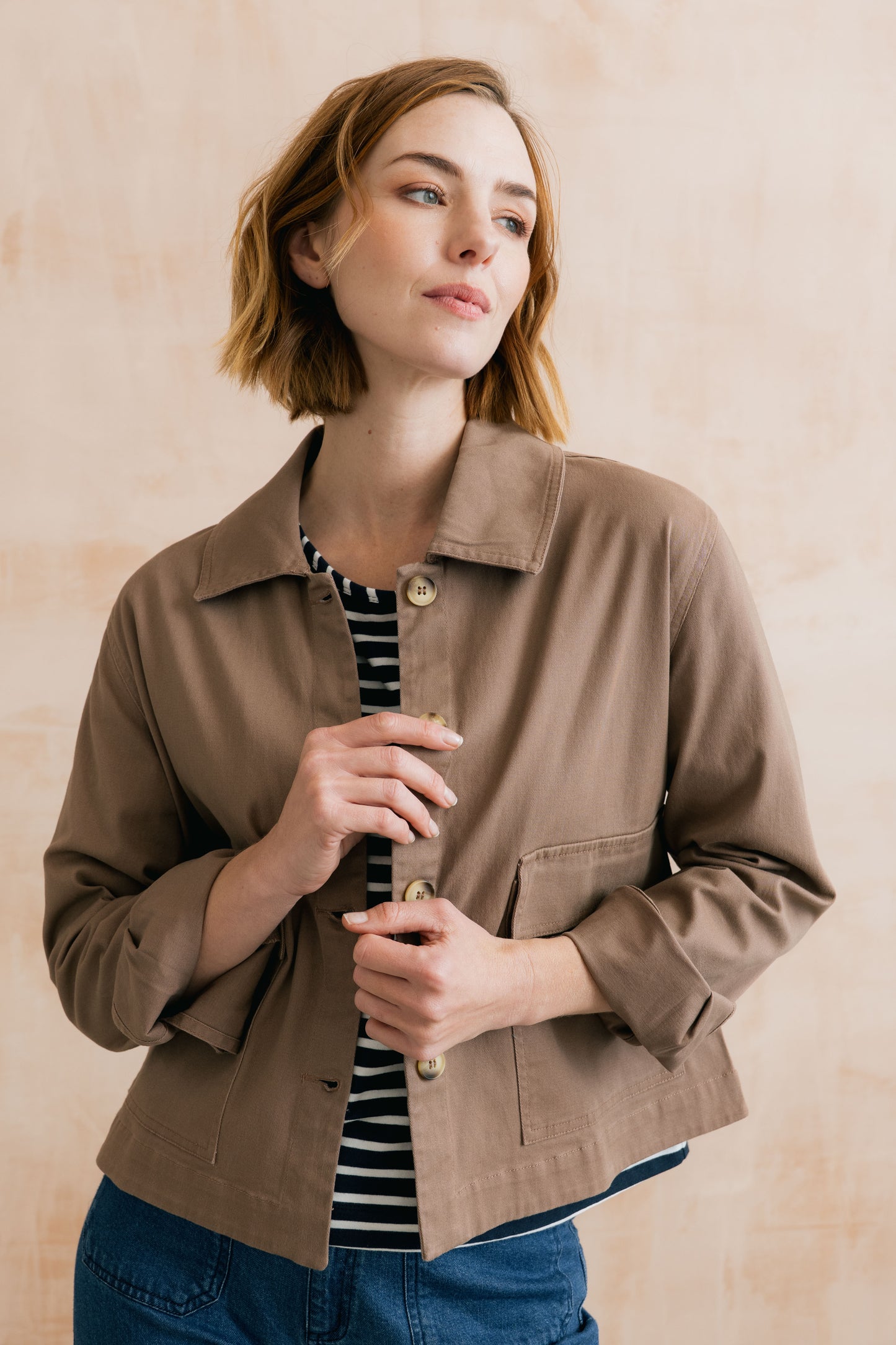 Woman wearing a brown jacket over a striped shirt with a neutral background