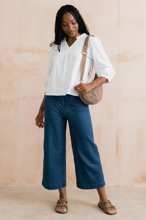 Woman wearing a white blouse and blue pants, holding a beige bag against a beige background
