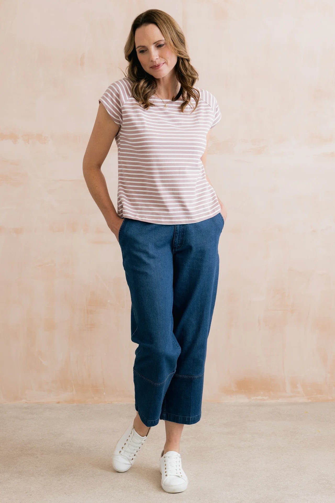 Woman wearing a striped shirt and blue pants against a beige background