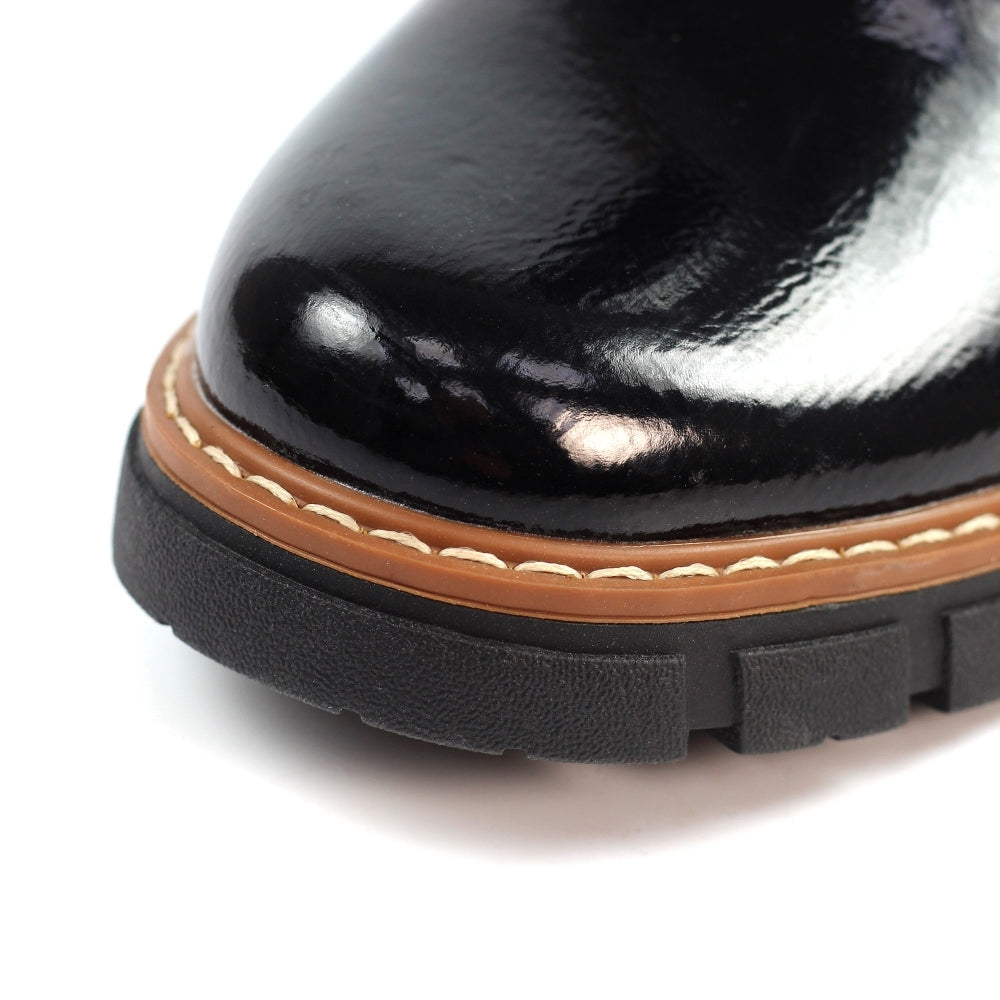 Close-up of a black patent leather shoe with a brown sole on a white background