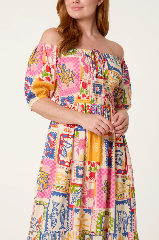 Woman wearing a colorful off-shoulder dress with a pattern of various shapes and colors on a white background.