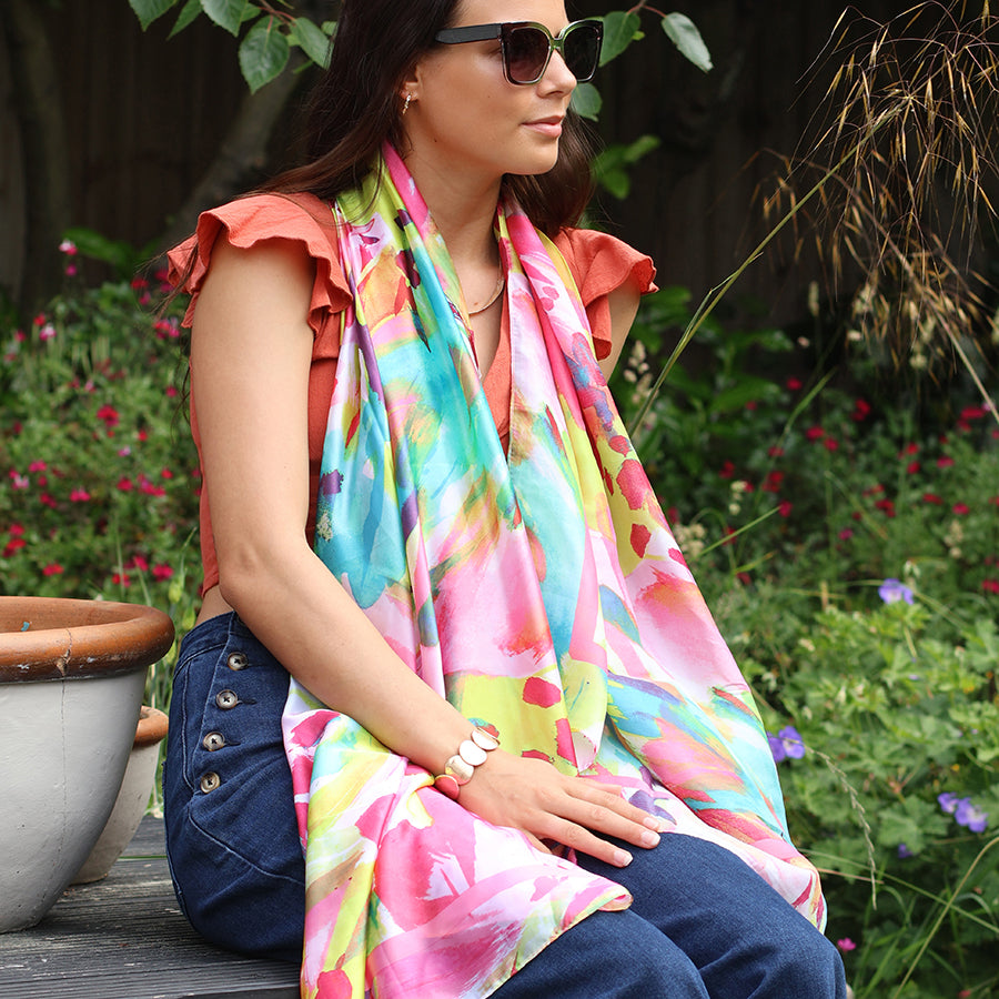 Woman sitting outdoors wearing a colorful scarf and sunglasses, with a garden background.