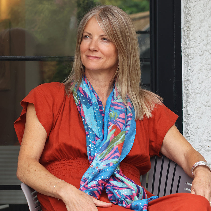 Woman wearing a colorful scarf and red top sitting outdoors.
