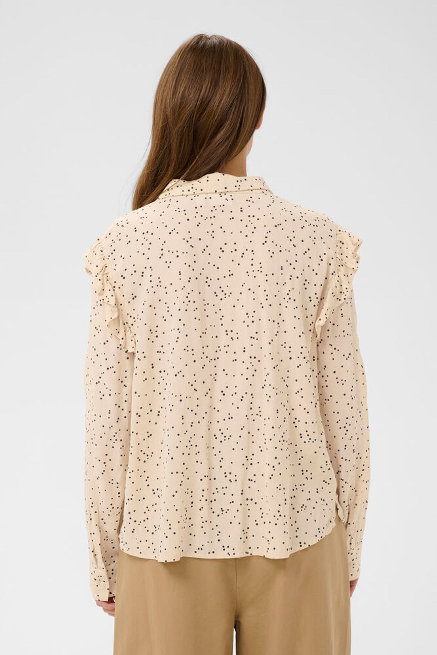 Woman wearing a beige floral blouse with a plain background