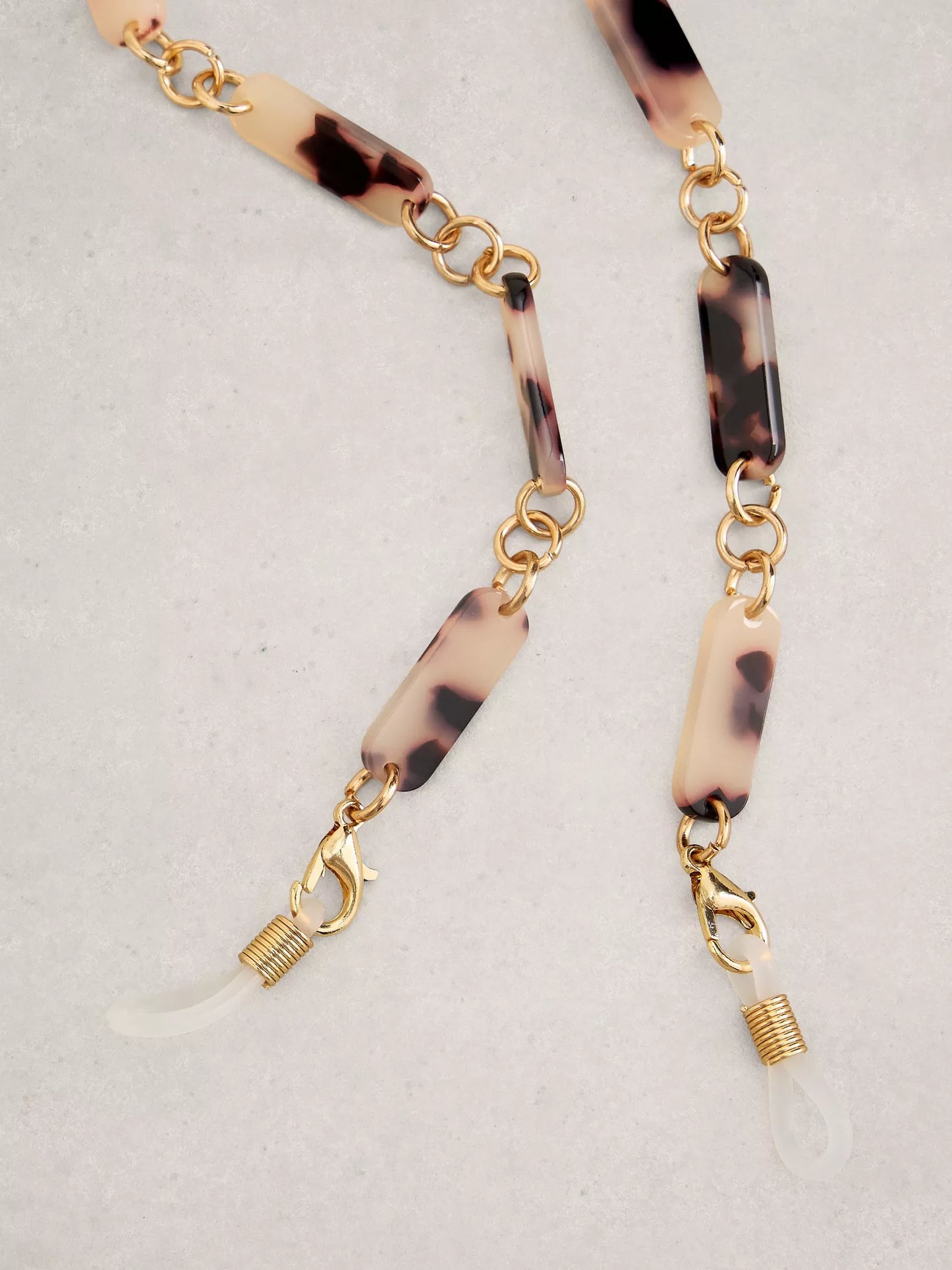 Gold and tortoiseshell sunglasses chain on a light gray background