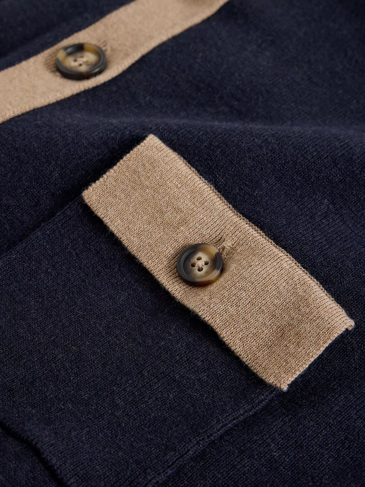 Close-up of a navy knit garment with contrasting beige trim and decorative buttons.