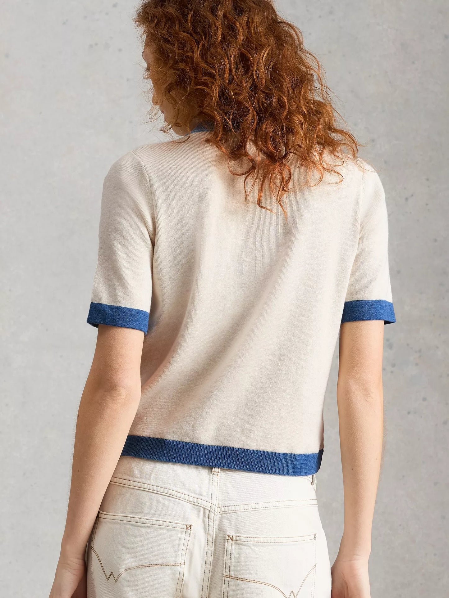 Person wearing a white sweater with blue trim against a gray background