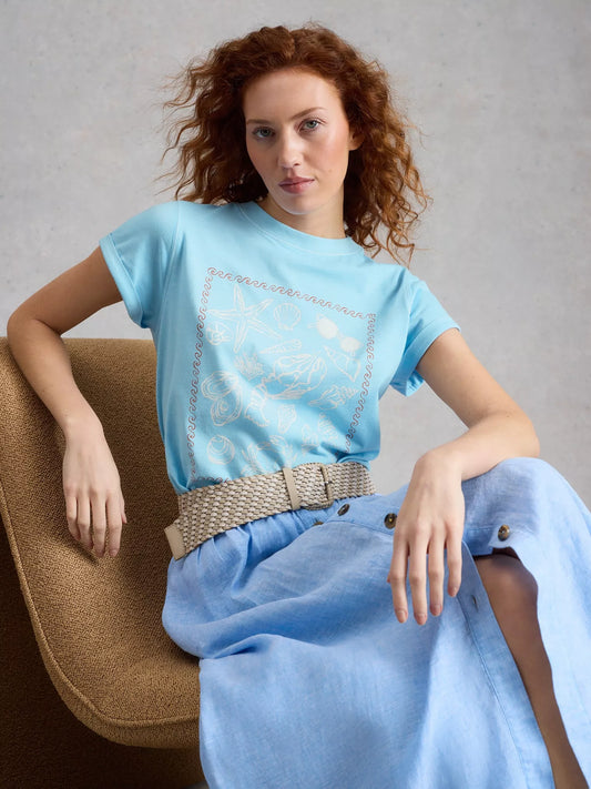 Woman wearing a light blue t-shirt and skirt sitting on a chair against a gray background