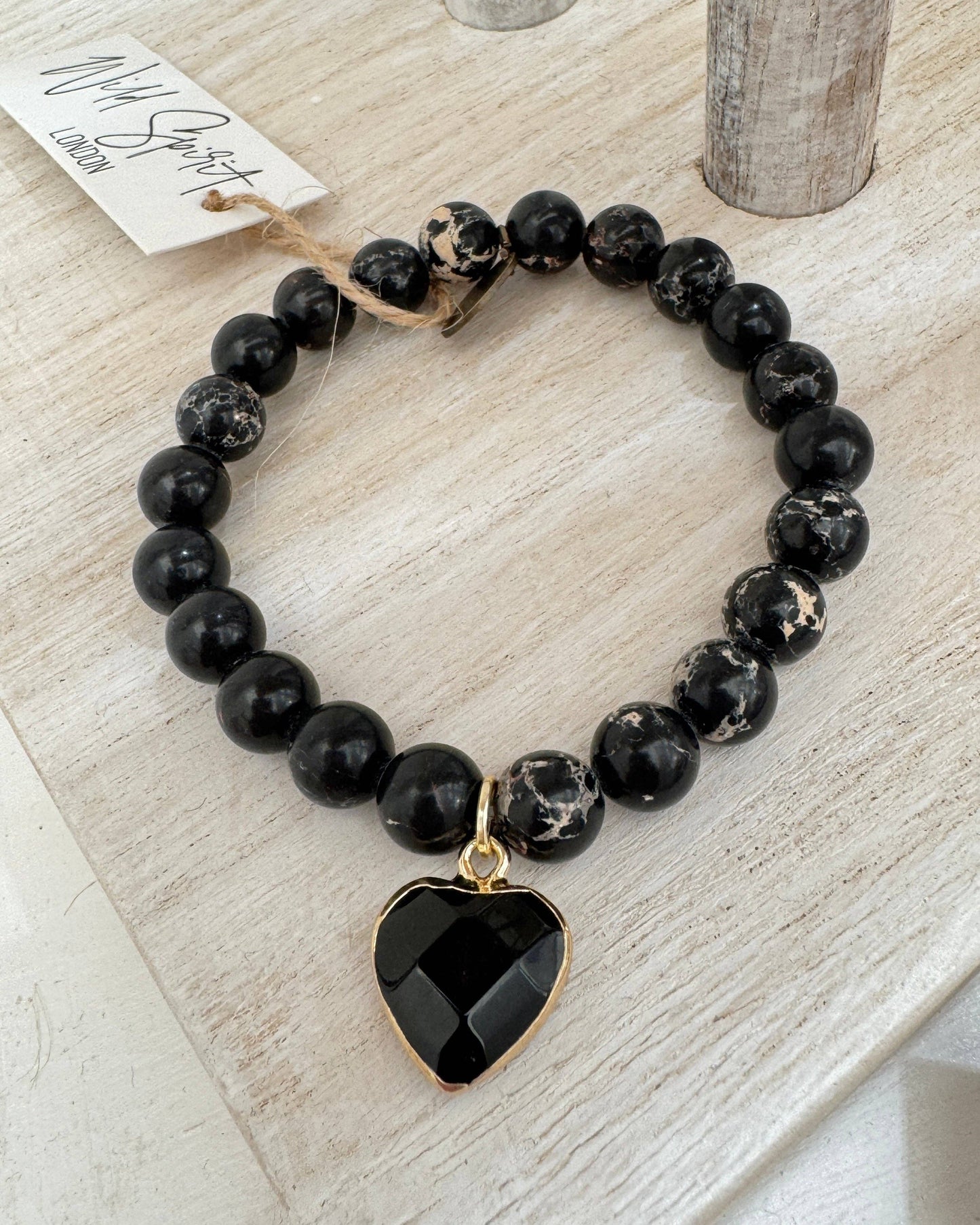 Black beaded bracelet with a heart-shaped black pendant on a light wooden surface.
