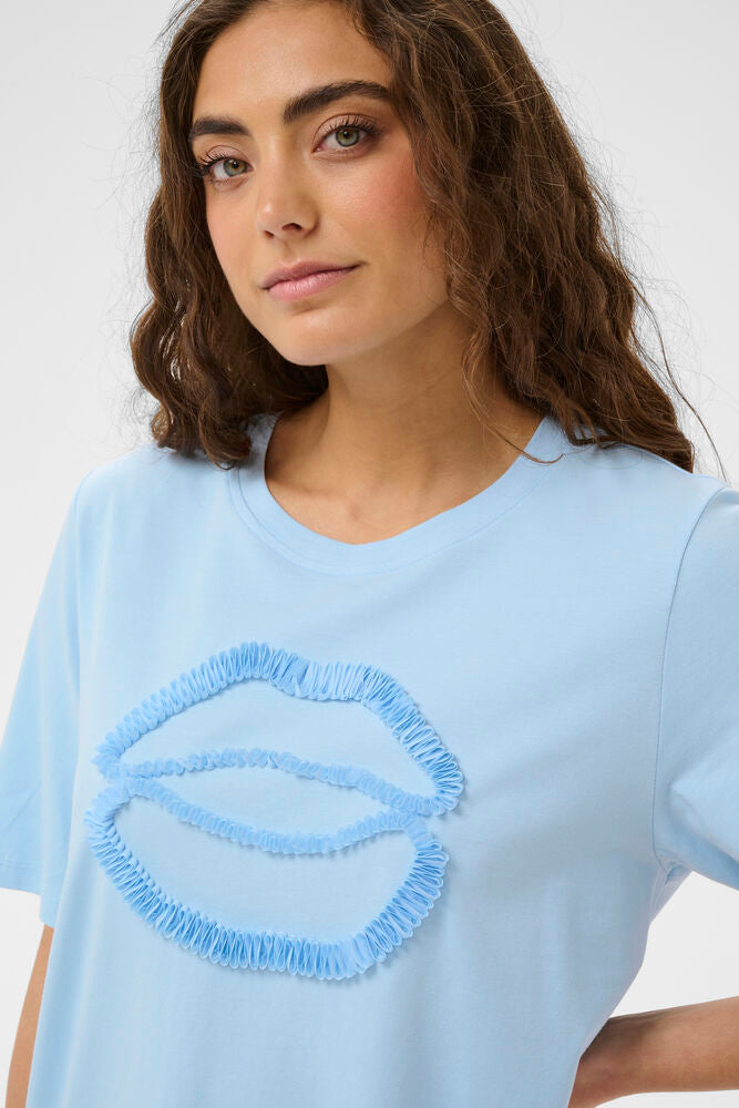 Woman wearing a light blue t-shirt with decorative trim on a plain background