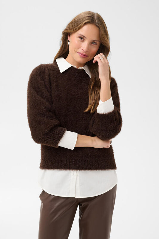 A woman modeling a dark brown fuzzy knit sweater with a white pointed collar and white cuffs, worn over a white collared shirt and brown pants, against a light gray studio background.