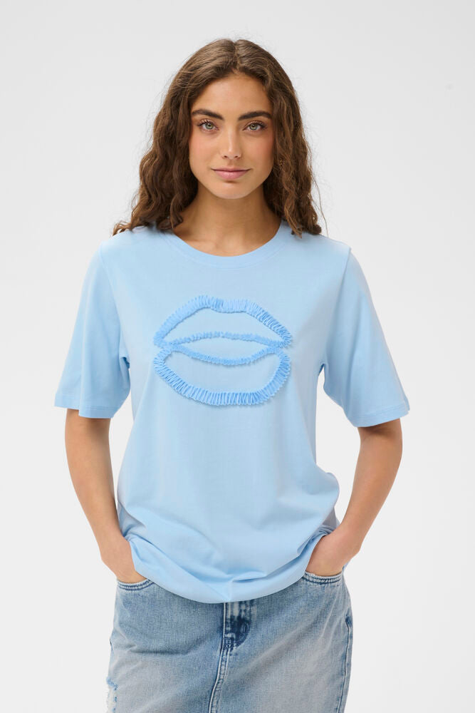 Woman wearing a light blue t-shirt with a graphic design on a plain background