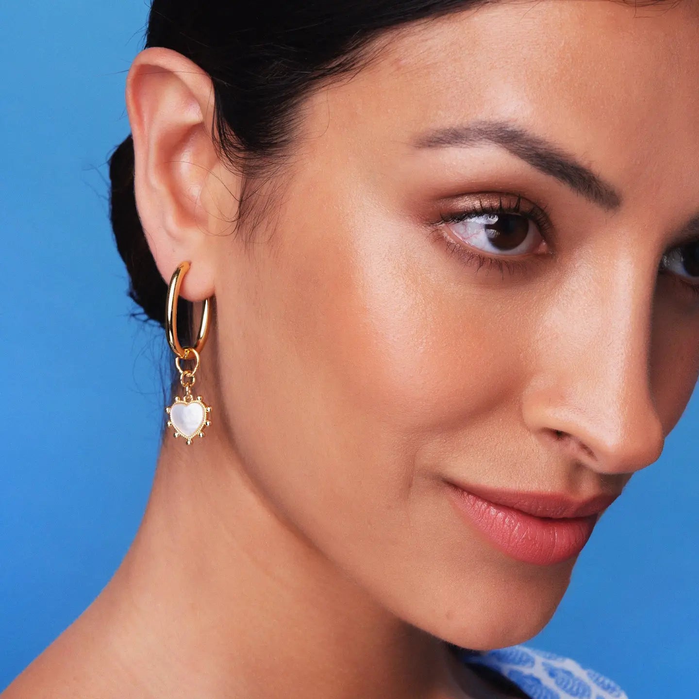 Close-up of a woman wearing gold hoop earrings with a blue background