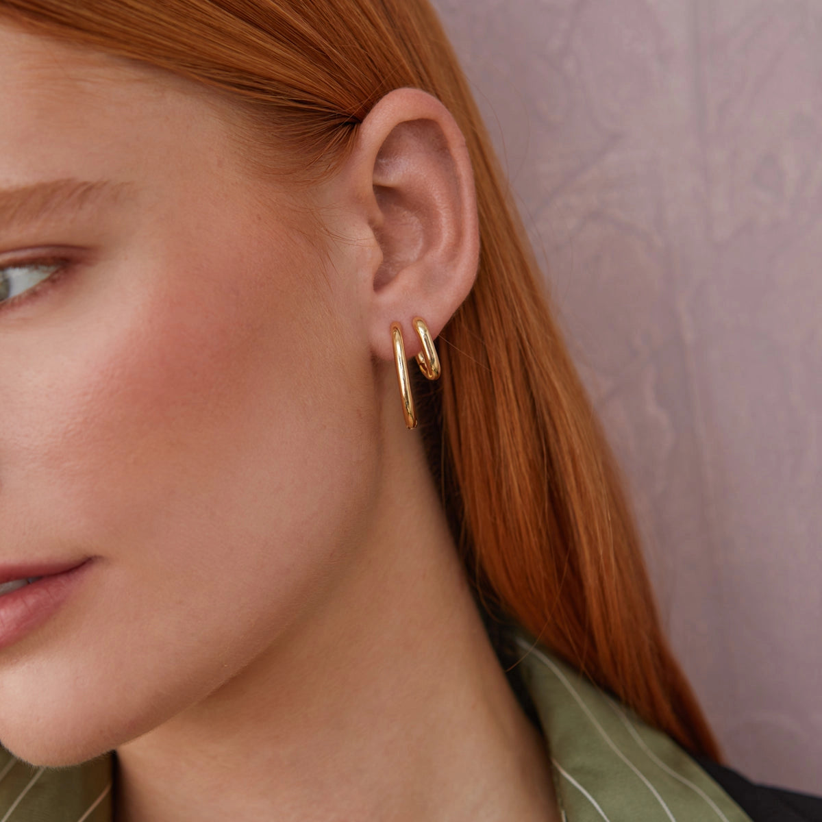 Close-up of a person wearing a gold hoop earring against a neutral background
