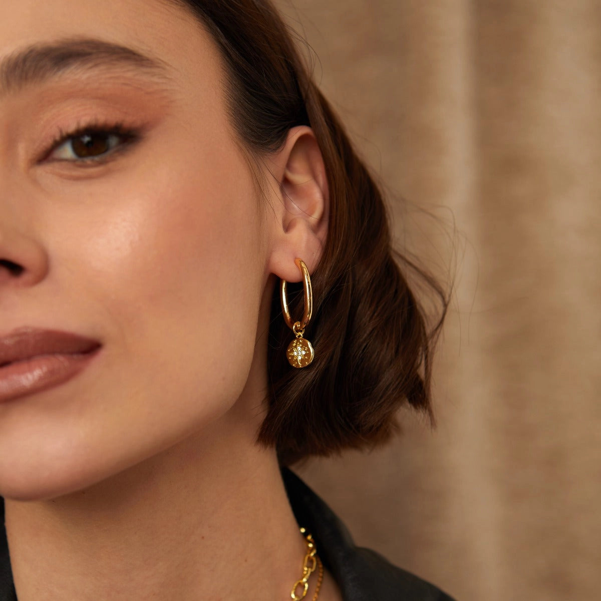 Close-up of a woman wearing gold hoop earrings with a neutral background