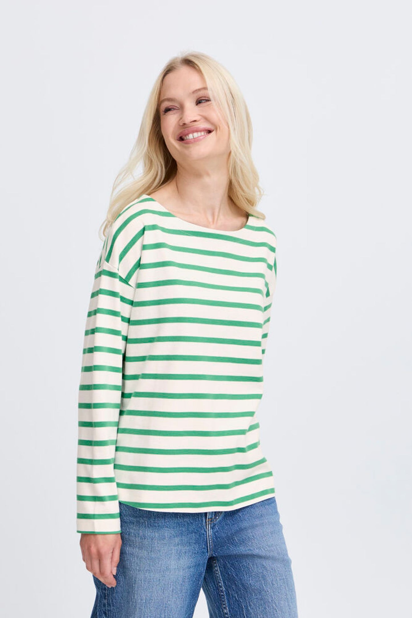 Woman wearing a green and white striped long-sleeve shirt and blue jeans on a light gray background