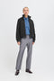 Person wearing a black jacket, blue shirt, gray pants, and black shoes on a white background