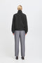 Person wearing a dark gray turtleneck sweater and light gray pants on a white background