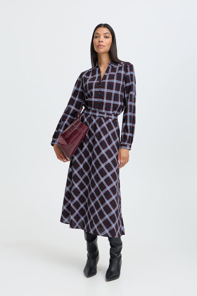 Woman wearing a plaid dress holding a red bag on a white background