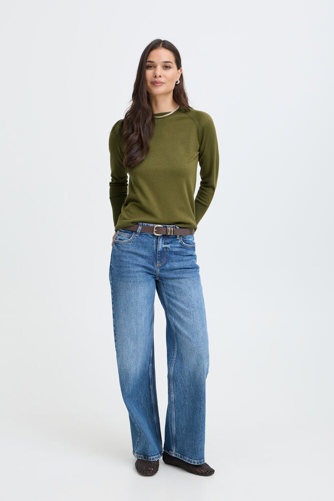 A woman modeling a ribbed olive green long-sleeve top and wide-leg blue jeans with a brown belt, standing against a light gray studio background.