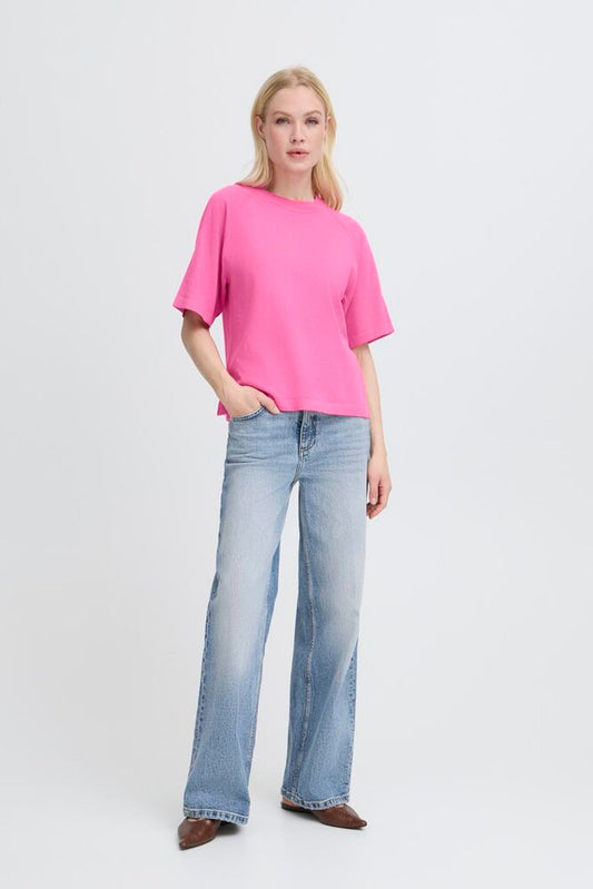 Woman wearing a bright pink top and light blue jeans on a white background