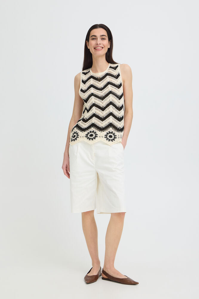 Woman wearing a sleeveless black and white patterned top with white shorts on a white background