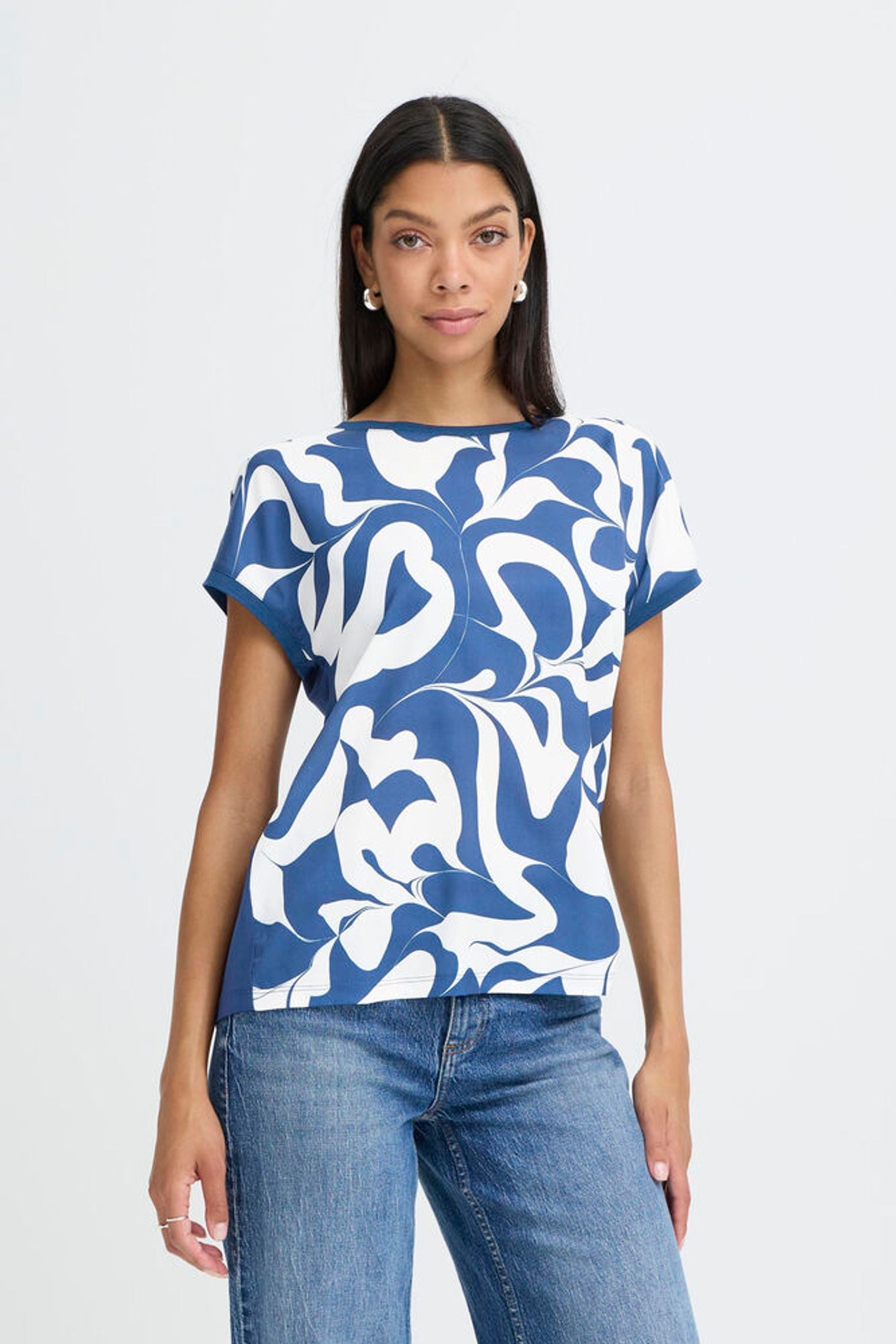 Woman wearing a blue and white patterned top with jeans on a light gray background