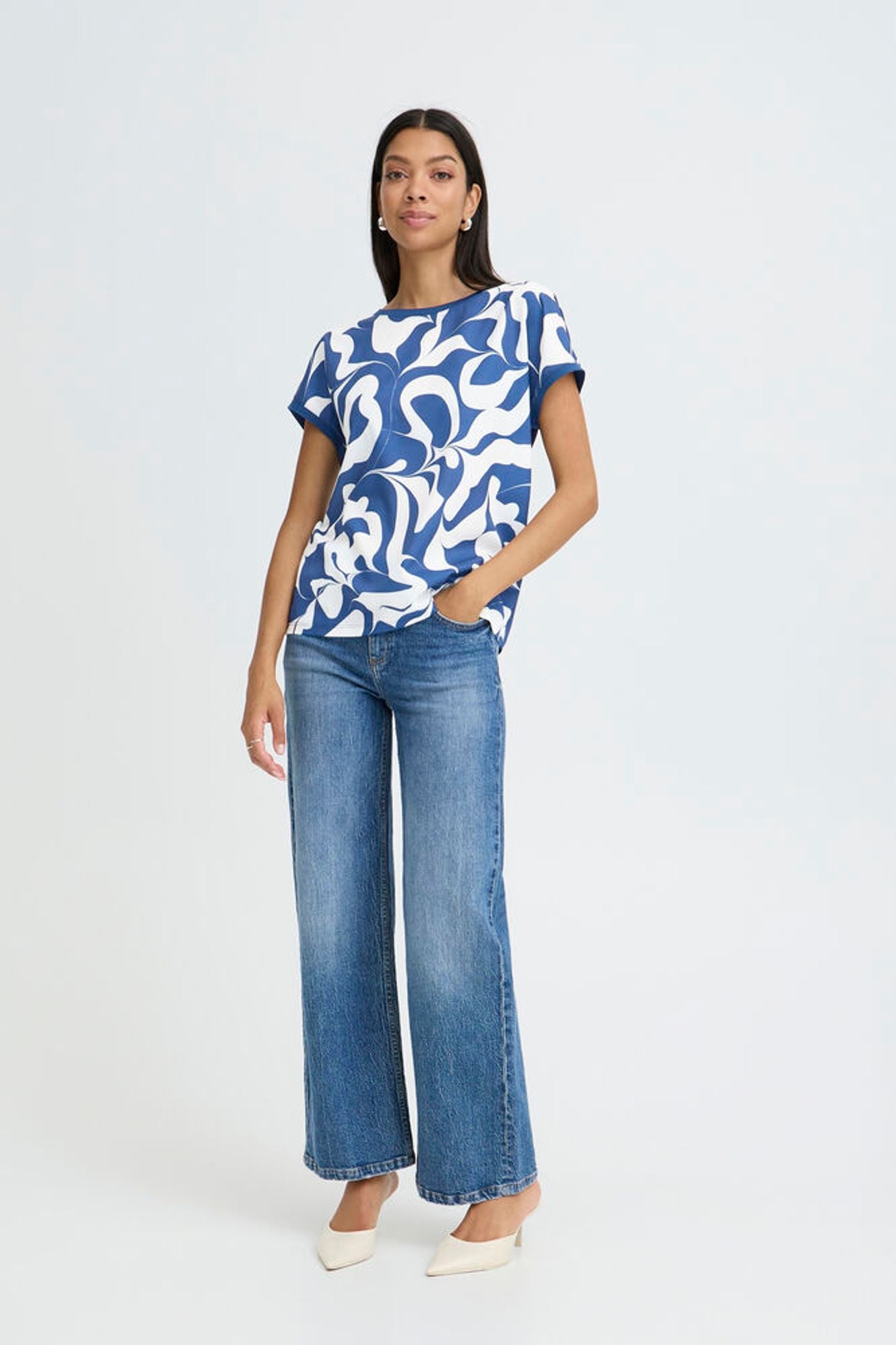 Woman wearing a blue and white patterned top with wide-leg jeans on a white background
