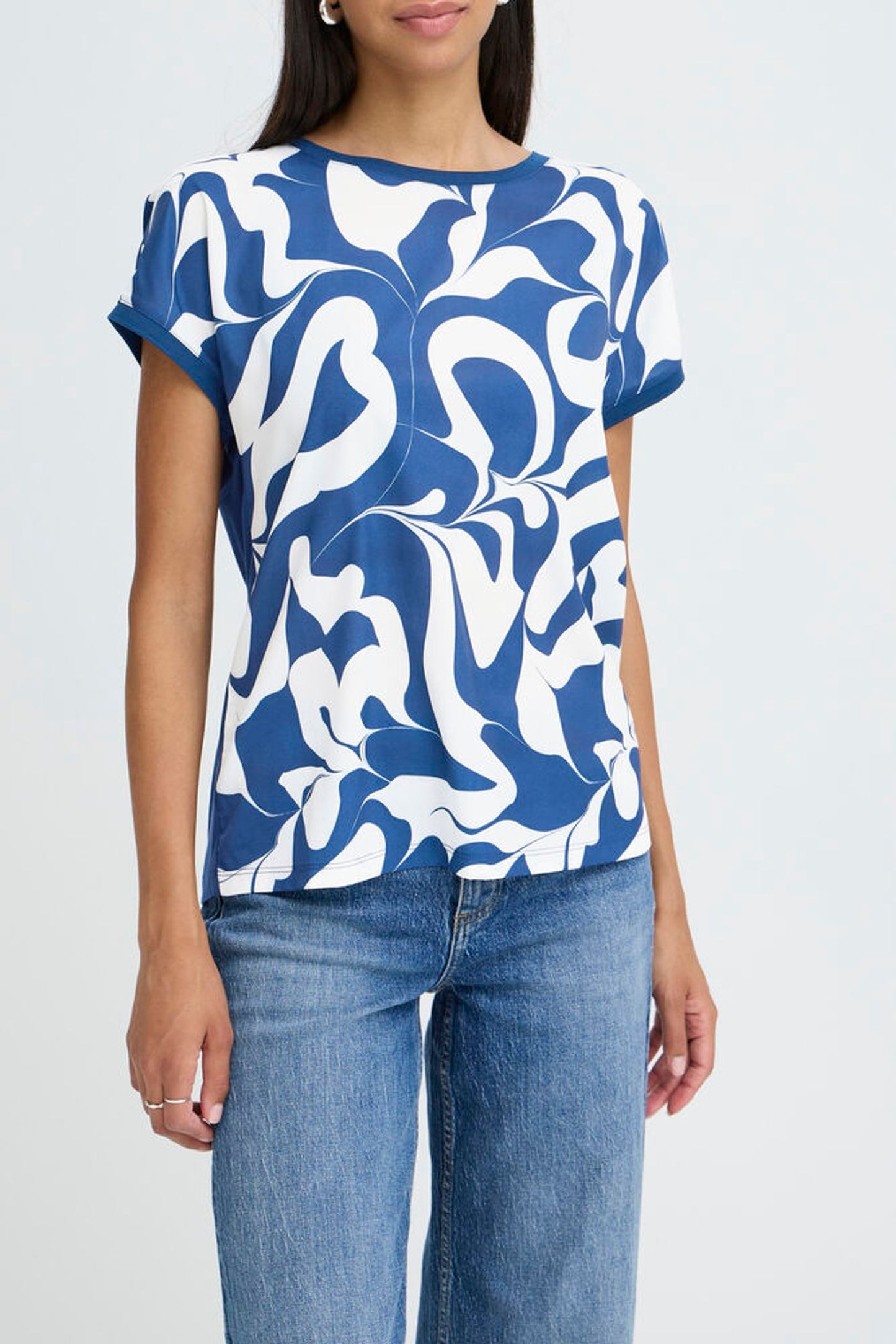 Woman wearing a blue and white patterned top with jeans on a light gray background