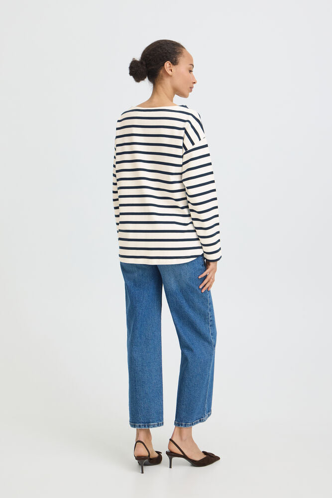 A woman shown from the back wearing a navy and white horizontally striped long-sleeve top, blue jeans, and black pointed-toe heels against a plain light gray studio background.
