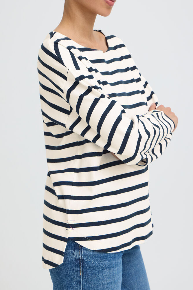 A woman wearing a cream and navy blue horizontally striped long-sleeve top with blue jeans, shown from the side against a light gray background.