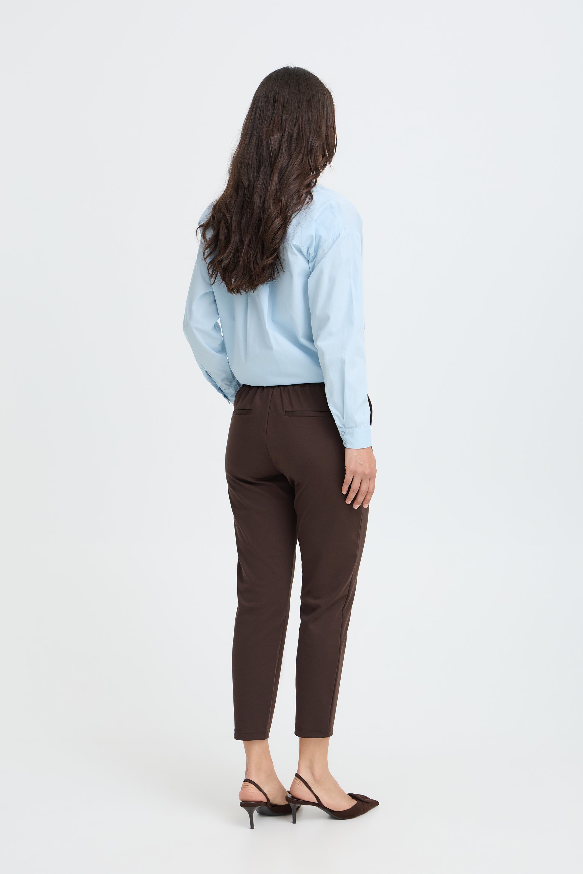 Back view of model wearing chocolate brown tapered trousers
