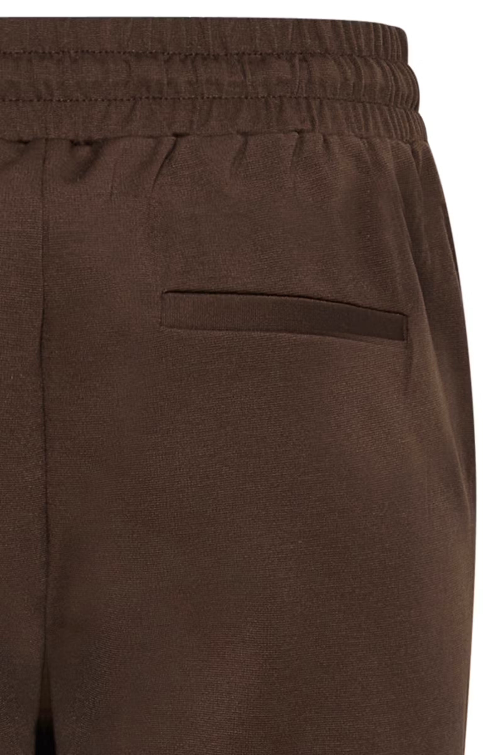 Close-up of dark brown trousers showing the elastic waistband and a side welt pocket.