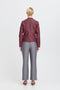Person wearing a burgundy jacket and grey pants on a white background