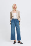 Woman wearing a beige blazer, white top, and blue jeans on a white background