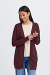 Woman wearing a burgundy cardigan over a white shirt and blue jeans on a light gray background