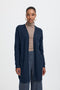 Woman wearing a navy cardigan over a beige turtleneck and gray pants on a white background