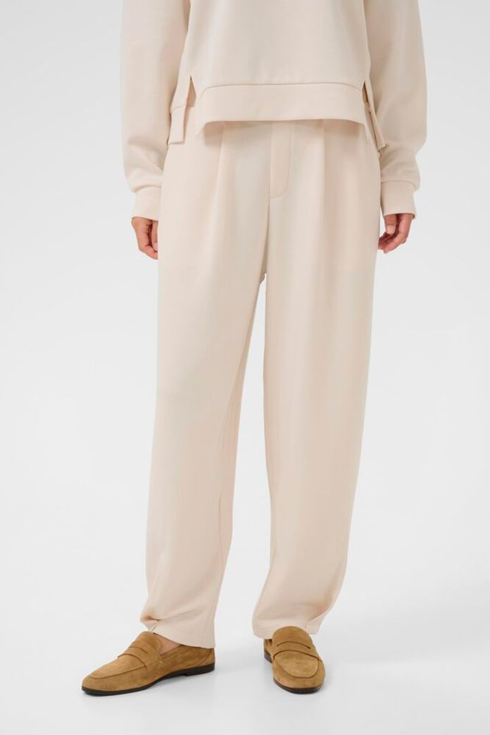 Person wearing a beige outfit with pants and a top on a white background