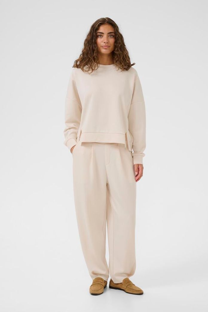 Woman wearing a beige sweater and pants set on a white background