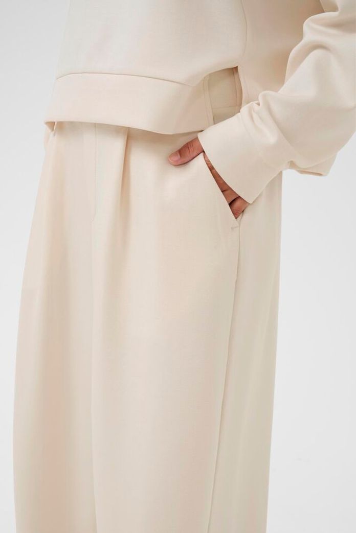 Close-up of a person wearing a beige coat with a plain background