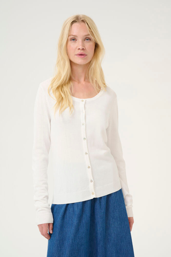 Woman wearing a white cardigan and blue skirt against a plain background