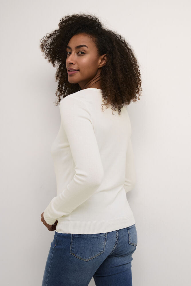 Woman wearing a white cardigan and blue jeans against a plain background