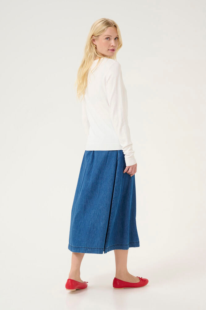 Woman wearing a white cardiagn and blue skirt on a white background