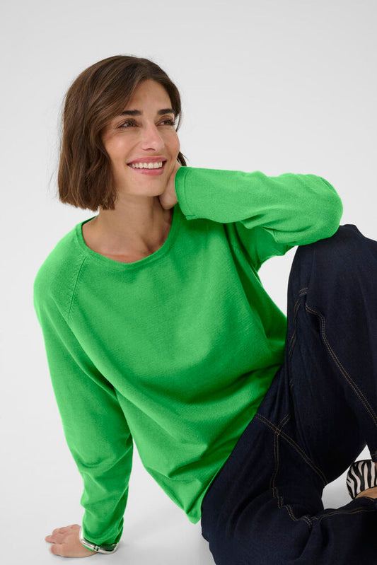 Woman wearing a bright green sweater and dark pants against a white background